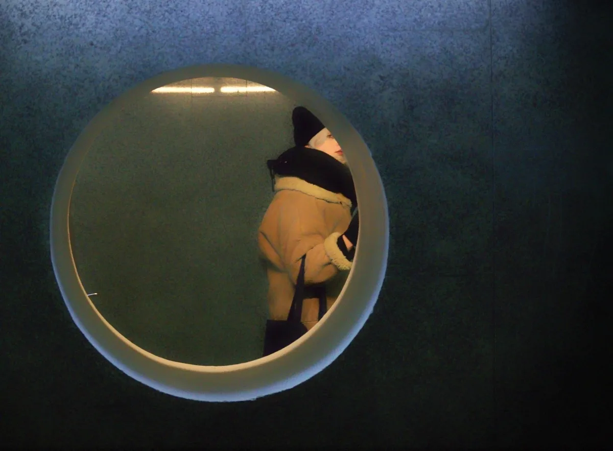 Person in a winter coat seen through a round window in a dark wall